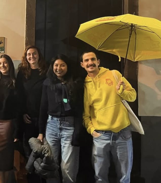 Pedro in a yellow Good Ground hoodie holding a yellow umbrella, with guests on a night out in Funchal