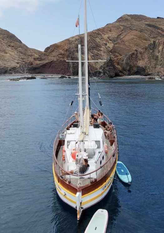 Traditional wooden sailing boat anchored in a bay in Madeira with paddleboards alongside