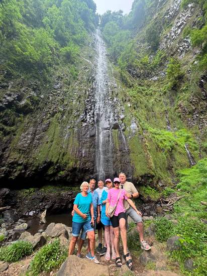 Hikers at the base of a tall waterfall in Madeira