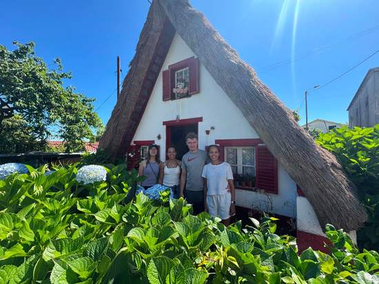 Guests in front of a traditional triangular thatched house in Santana, Madeira